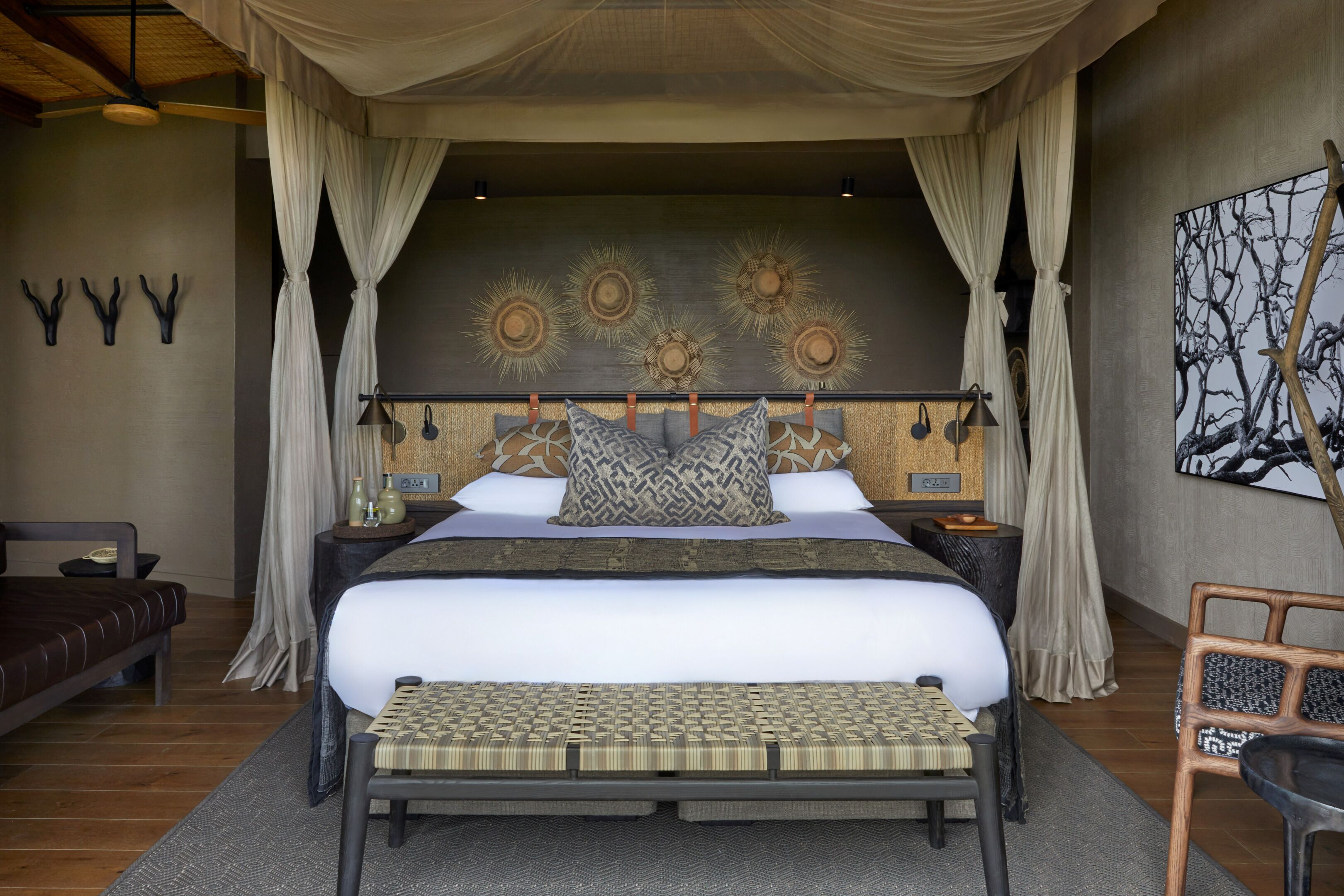 Une chambre à coucher avec un lit à baldaquin, un banc, une chaise et un mur orné de motifs décoratifs en forme de soleil.