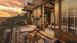 A modern outdoor living area with a wooden deck, lounge chairs, and a glass-enclosed room with a view of the landscape.