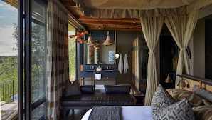 A bedroom with a large bed, a seating area, a vanity, and a view of the outdoors.