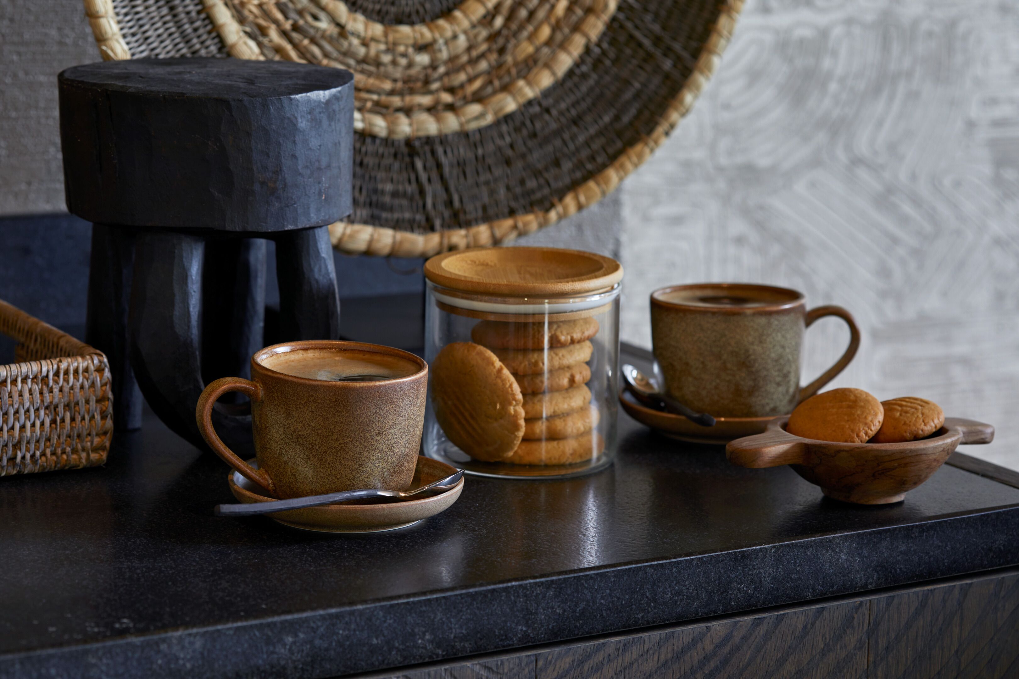 A coffee setup with a cup, saucer, and a wooden mug on a dark countertop.