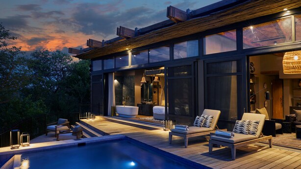 A modern outdoor pool area with lounge chairs and a hot tub, surrounded by a wooden deck and glass walls.
