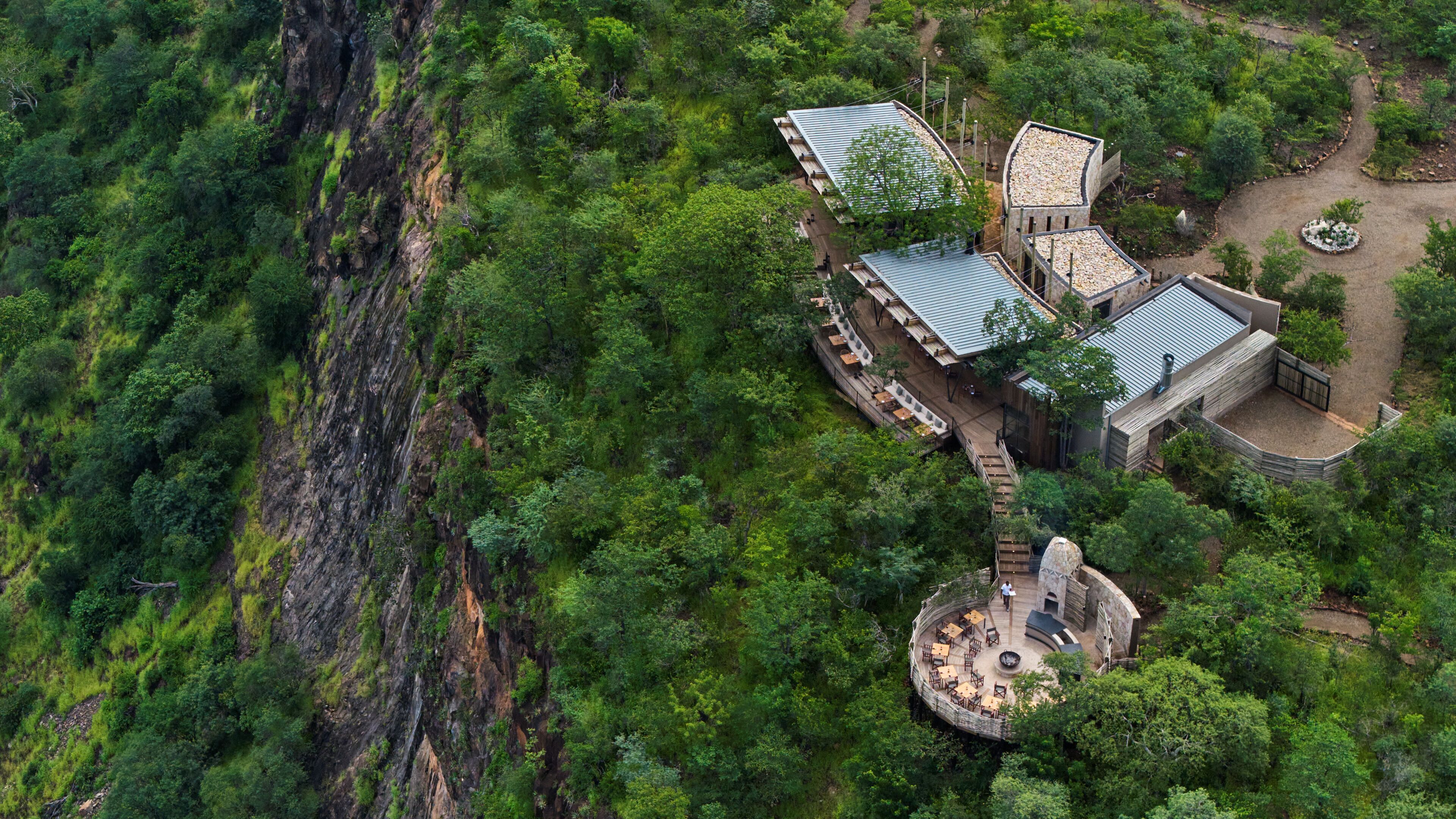 A circular building with a central courtyard surrounded by wooden structures with sloped roofs, set in a lush, forested area.