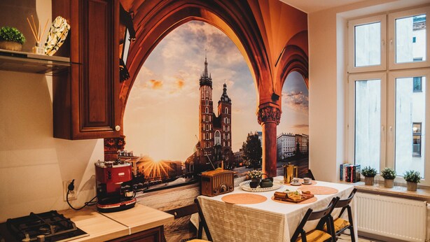 A kitchen with a large mural of a cityscape, a stove, and a dining table set for two. - FatCat Apartments (Kraków)