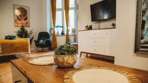 A wooden dining table with woven placemats, a potted plant, and a television on the wall. - FatCat Apartments (Kraków)