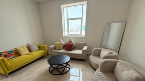 Sala de estar com um sofá amarelo, um sofá bege, uma mesa de centro redonda e uma janela com vista para a cidade.