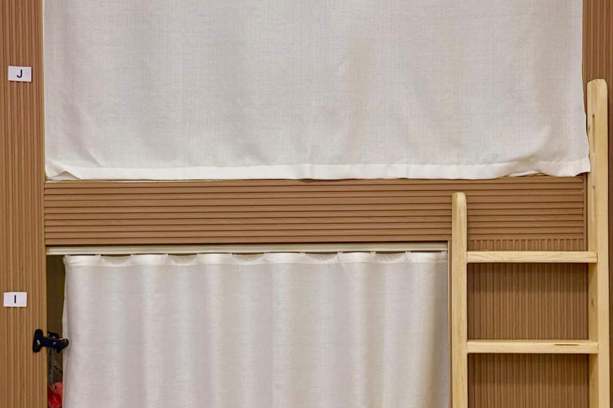 Una habitación con literas, una cortina y una escalera de madera.