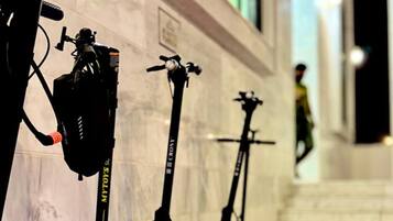 Tres patinetes eléctricos apoyados contra una pared, con una persona al fondo.