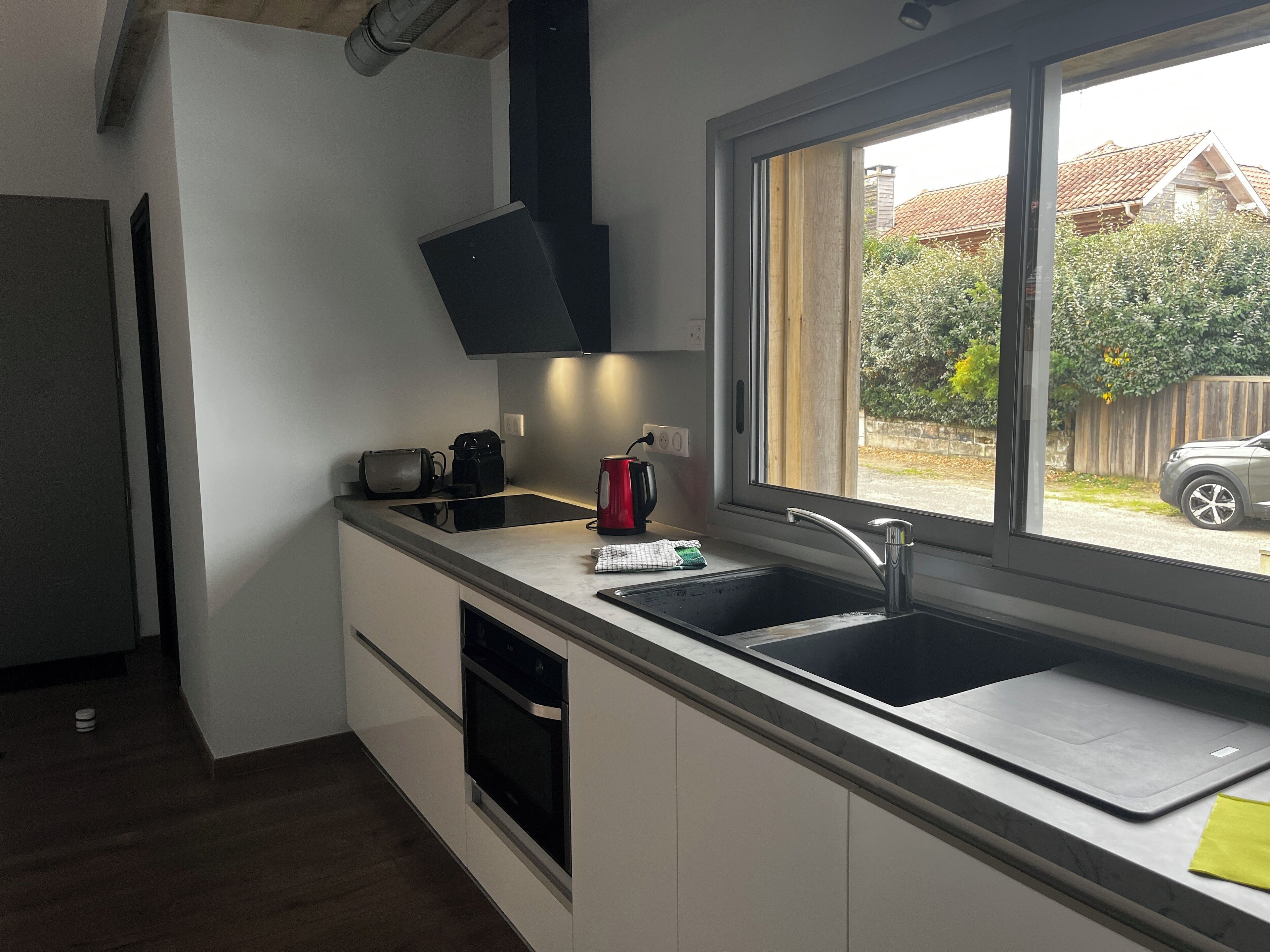 Une cuisine moderne équipée d’un four encastré, d’un évier et d’une fenêtre donnant sur un quartier résidentiel.