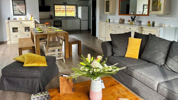 A modern living room with a grey sofa, wooden coffee table, and a dining area with a wooden table and chairs.