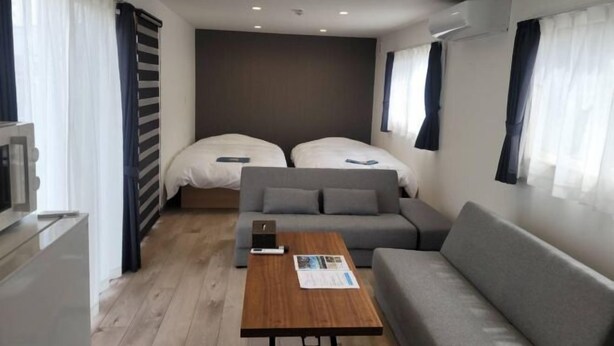 A compact hotel room with two beds, a sofa, a small table, and a TV. - Toya Center Village (Toyako)