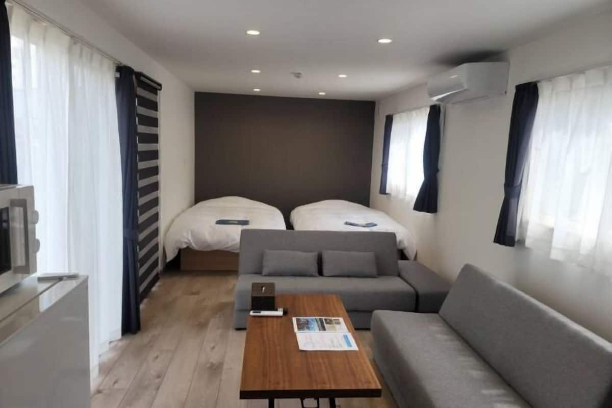 A compact hotel room with two beds, a sofa, a small table, and a TV.