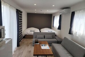 Une chambre d’hôtel de taille modeste, équipée de deux lits, d’un canapé, d’une petite table et d’un téléviseur.