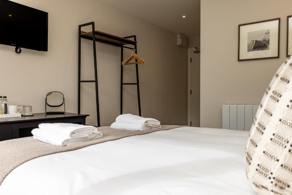 A hotel room with a bed, a desk with a mirror, a TV mounted on the wall, and a radiator.