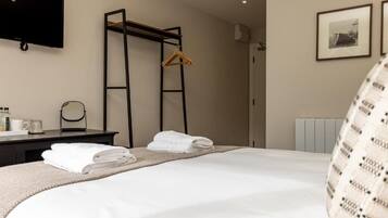 A hotel room with a bed, a desk with a mirror, a TV mounted on the wall, and a radiator.