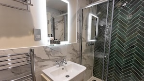 A modern bathroom with a marble sink, a glass shower enclosure, and a mirror above the sink. - The Town Crier (Tenby)