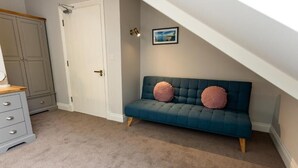 A room with a blue sofa, two pink cushions, a wooden dresser, and a white door. - The Town Crier (Tenby)