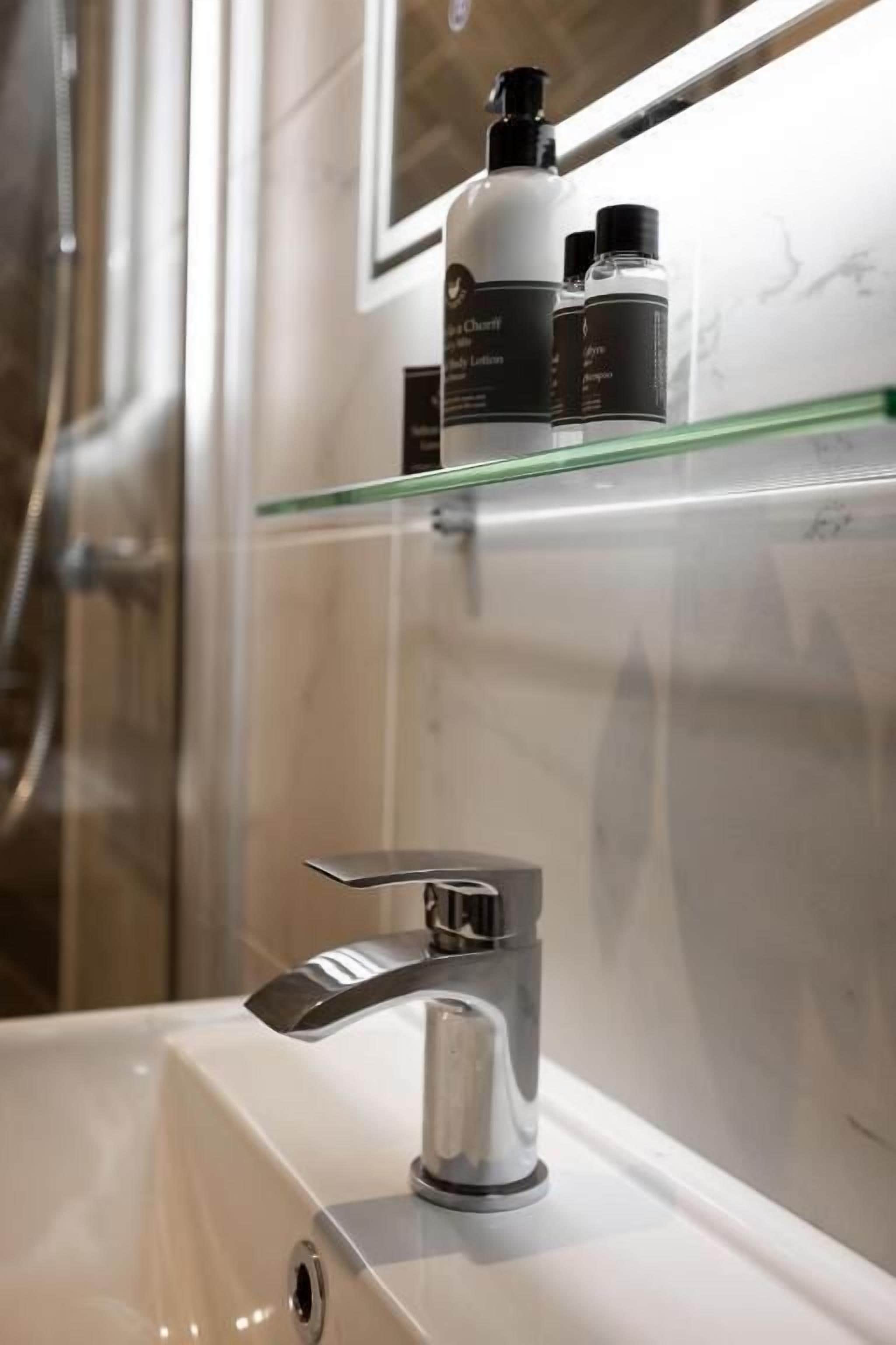 A bathroom with a white sink, a glass shelf with toiletries, and a shower area.