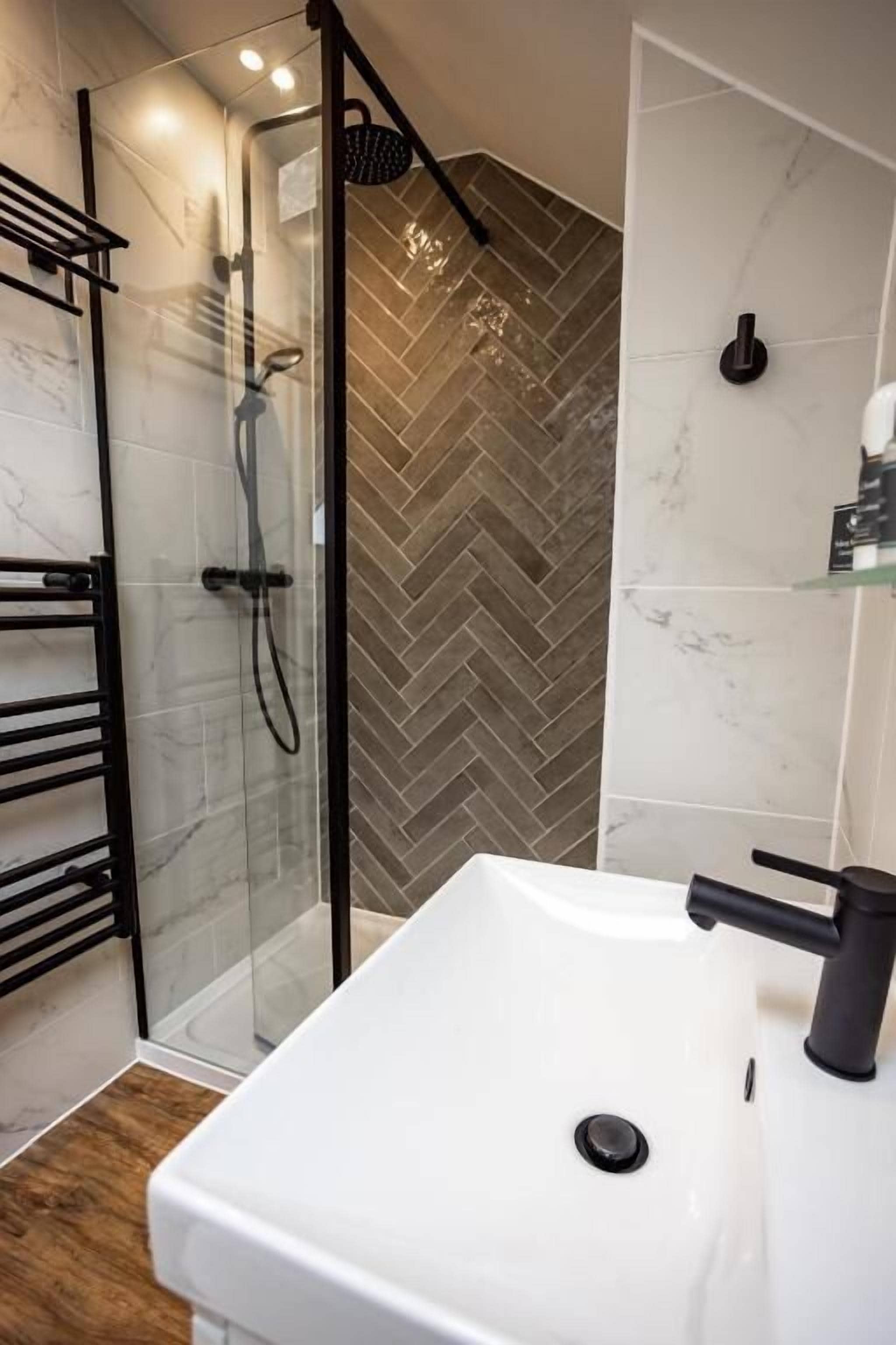 Un baño moderno con ducha envuelta en vidrio, un lavamanos blanco y baldosas con patrón de espiga.