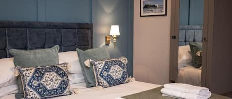 Habitación de hotel con una cama, dos almohadas, una mesita de noche con lámpara, una toalla doblada sobre la cama y un armario.