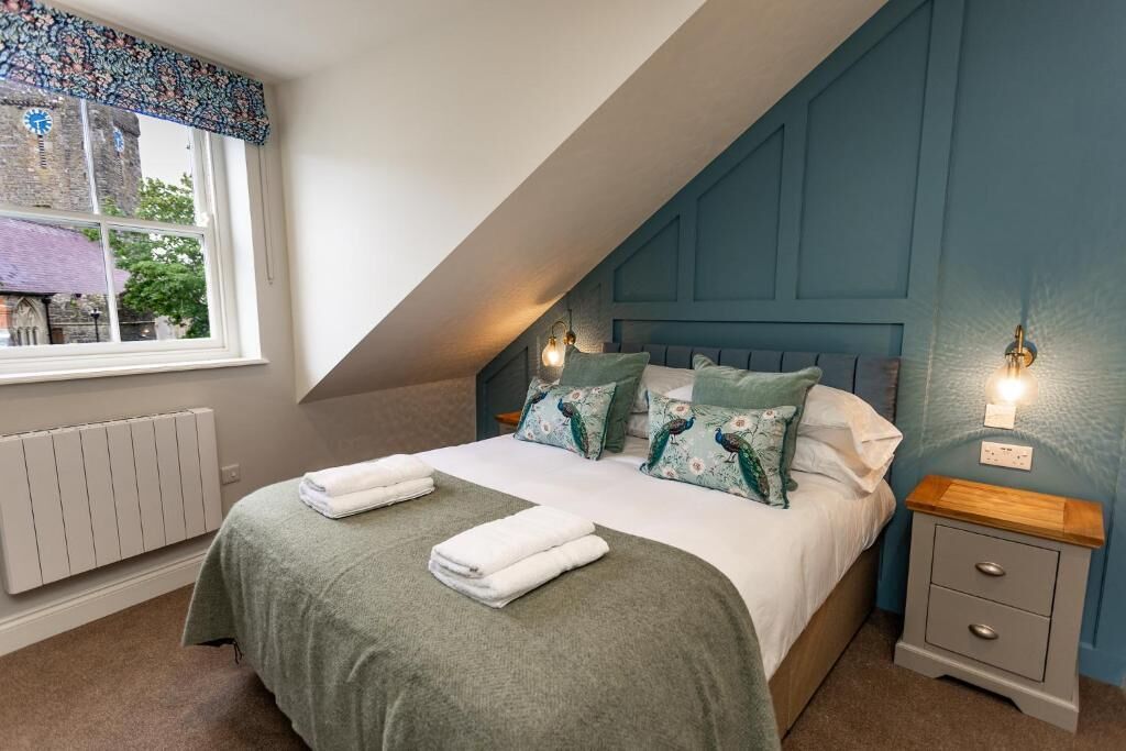 Une chambre à coucher avec un lit, deux tables de chevet, une fenêtre donnant sur un immeuble et un radiateur.