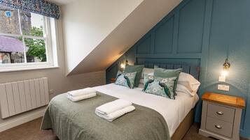 Une chambre à coucher avec un lit, deux tables de chevet, une fenêtre donnant sur un immeuble et un radiateur.