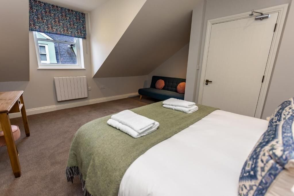 A bedroom with a bed, a chair, a window with a curtain, and a door.