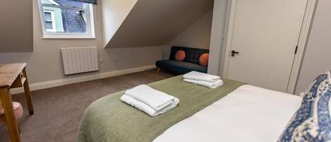 A bedroom with a bed, a chair, a window with a curtain, and a door.