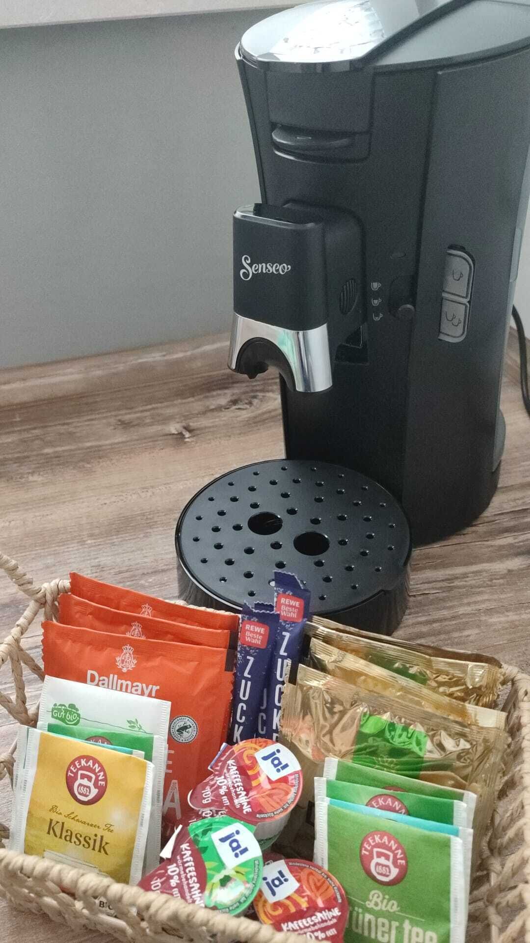 Une machine à café, un panier de sachets de thé et une dosette de café.