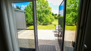 Eine Glastür öffnet sich zu einer Außenpatio mit Backsteinfußboden, einem Metalltisch und Stühlen.
