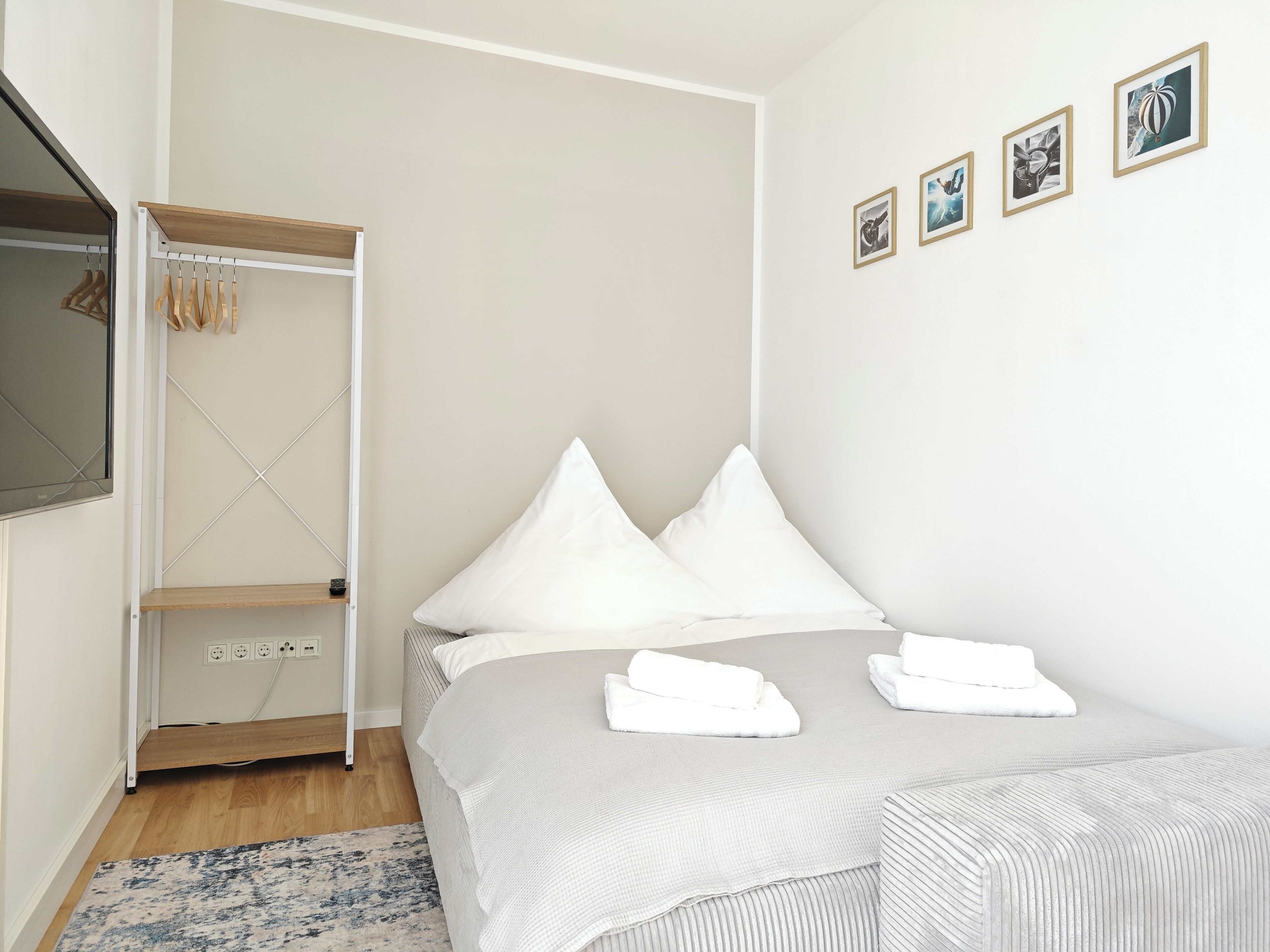 A neatly arranged bedroom with a bed, a wardrobe, and a wall-mounted TV.