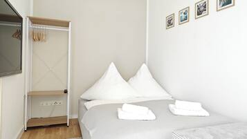 A neatly arranged bedroom with a bed, a wardrobe, and a wall-mounted TV.