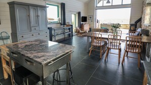 Een ruime keuken met een groot eiland, houten stoelen en een stenen open haard.