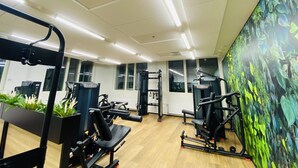 Une salle de sport équipée de divers appareils d’exercice, dotée de grandes fenêtres et ornée d’une fresque murale.