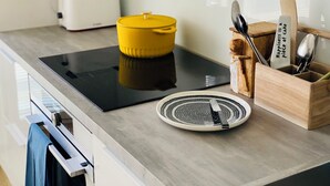 Une cuisine moderne avec une plaque de cuisson à induction noire, une casserole jaune, un grille-pain et des supports à ustensiles en bois.