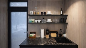 Cozinha compacta com bancada preta, pia e prateleiras com diversos utensílios de cozinha.