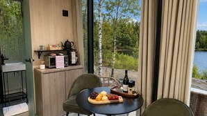 Ein modernes Zimmer mit Esstisch, Stühlen, Küchenzeile und einem großen Fenster mit Seeblick.
