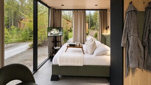 Ein modernes Schlafzimmer mit einem Bett, einem Nachttisch, einem Fernseher und Blick ins Freie.