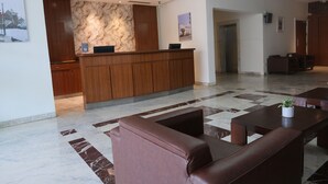 A reception area with a marble wall, wooden reception desk, and seating area with a potted plant. - DEVENTURE HOTEL (New Delhi)