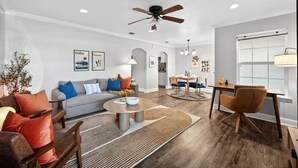 A modern living room with a grey sofa, a coffee table, and a dining area with a table and chairs. - Walk to AT&T Stadium | Modern 2BR With Backyard (Arlington)