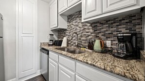 A kitchen with white cabinets, a granite countertop, a tiled backsplash, and modern appliances including a coffee maker and a kettle. - Walk to AT&T Stadium | Modern 2BR With Backyard (Arlington)