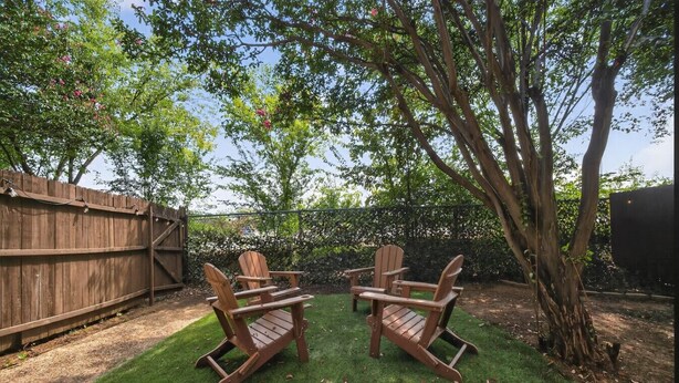 A backyard with a wooden deck, two Adirondack chairs, and a tree. - Walk to AT&T Stadium | Modern 2BR With Backyard (Arlington)