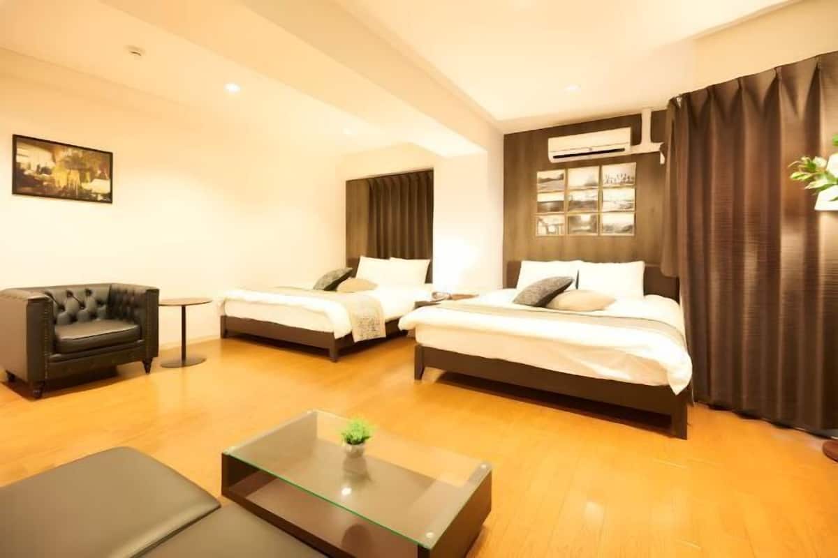 A hotel room with two beds, a sofa, a glass coffee table, and a painting on the wall.