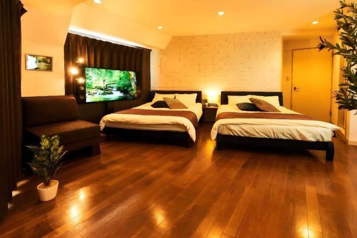A hotel room with two beds, a TV, a sofa, and a potted plant.