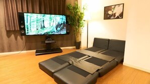 A modern living room with a flat-screen TV, a sofa, a coffee table, and a potted plant. - S’CASA Nishishinjuku (Tokyo)