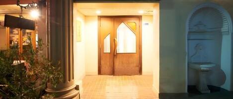 A hotel entrance with a tiled floor, a wooden door, and a stone statue.