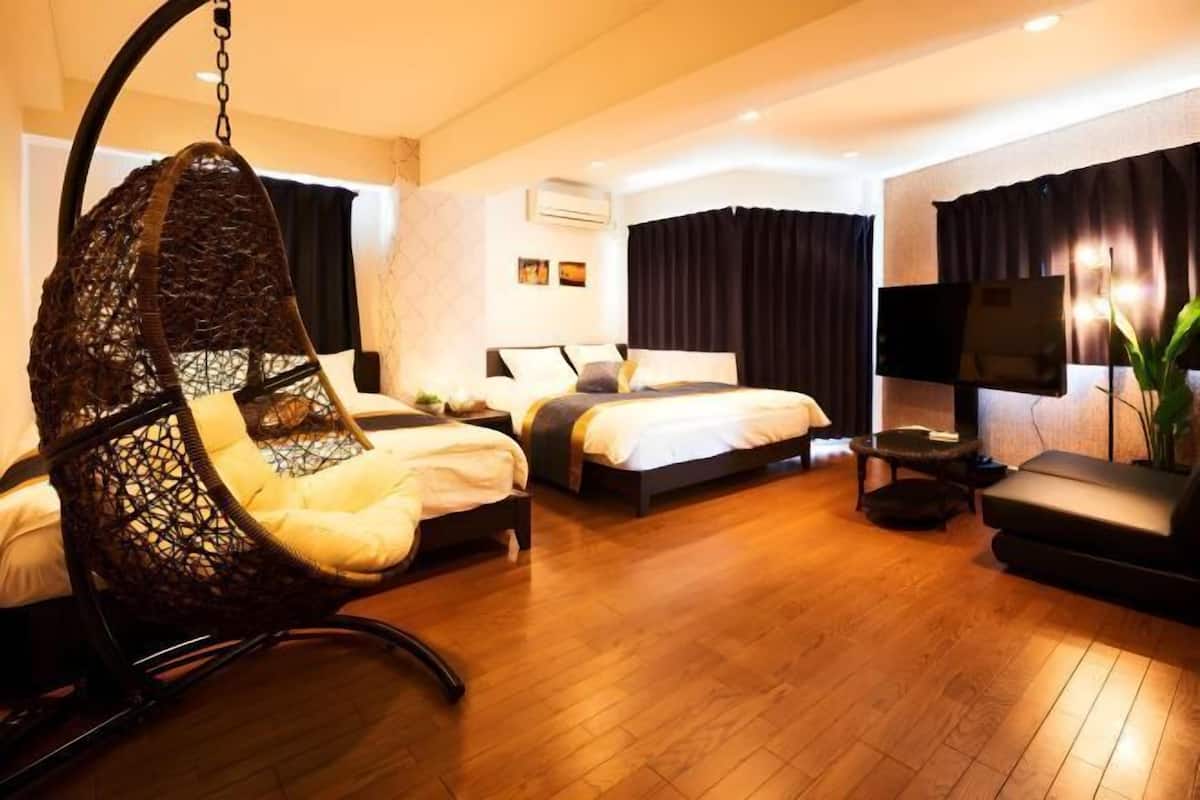 A hotel room with a hanging chair, two beds, a TV, and a plant.