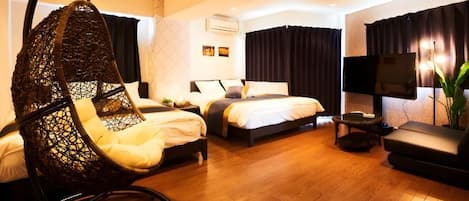 Une chambre d’hôtel avec un fauteuil suspendu, deux lits, une télévision et une plante.