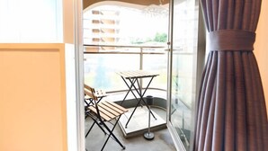 A balcony with a wooden table and chairs, a metal chair, and a view of buildings in the background. - S’CASA Nishishinjuku (Tokyo)