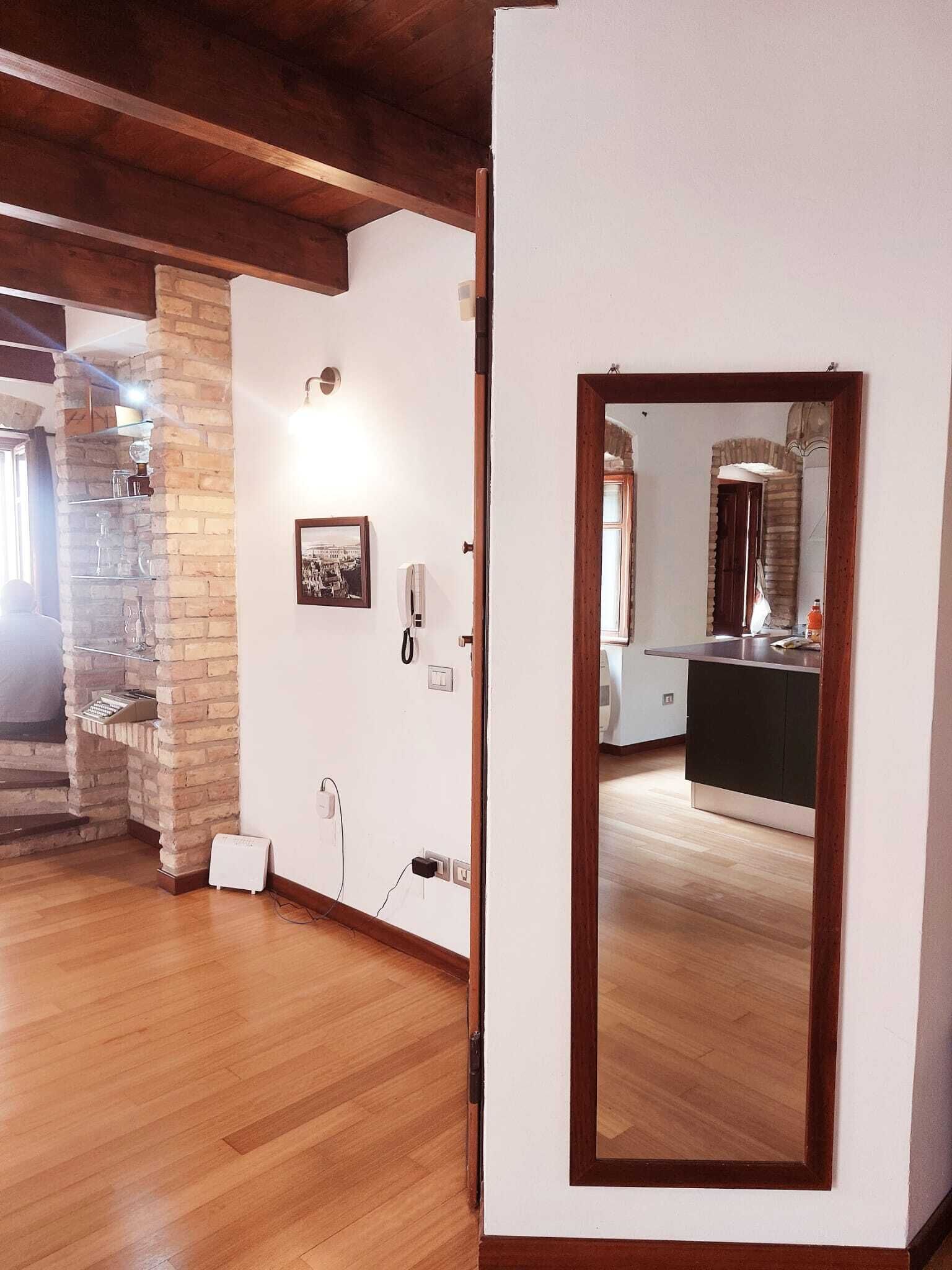 A spacious room with wooden flooring, a stone accent wall, a white door, and a mirror reflecting a kitchen area.