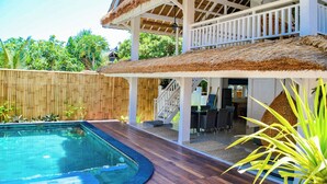 Ein Poolbereich mit Holzterrasse, einem strohgedeckten Gebäude und einem Bambuszaun.